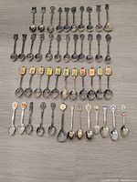 Top-down photo showing 37 silver plated collectible spoons including Hummel and Christmas spoons arranged in rows on a table.