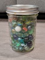 Front view of the glass jar filled with assorted multi-colored glass marbles.