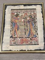 Frontal view of framed papyrus painting showing two Egyptian figures and signature at bottom left.