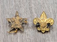 Two collectible vintage Boy Scouts pins. One is a star-shaped 'Be Prepared' sterling silver pin, the other a fleur-de-lis shaped Boy Scouts pin marked 'PAT 1911'.