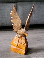 Front-left angle view of the eagle wood carving showing open wings and perched stance.