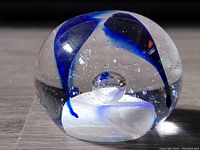 Close-up of the glass paperweight showing internal blue and white swirl design and bubble inside, along with signature on base.