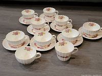 Front view of 8 Spode Rose Briar cup and saucer sets plus 2 additional cups arranged on floor, showing floral pattern and scalloped edges.