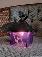 Front view of the Seagram's V.O. lantern bar light lit, showing purple translucent plastic with white branding and a black metal roof with hanging loop.