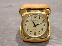 Full view of Westclox travel alarm clock in open tan folding case with gold trim.