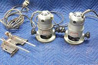 Two vintage Porter Cable routers with power cords and black adjustment knobs shown on a blue padded surface.