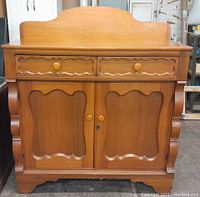 Front view of the antique poplar jelly cupboard showing two drawers, double doors with scalloped patterns and carved sides.