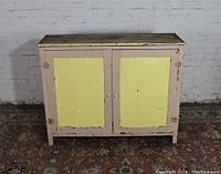 Front view of the antique jelly cupboard showing blush pink frame with pale yellow inset panels and distressed painted finish.