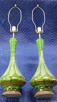 Photo showing front view of two green ceramic mid-century style table lamps side-by-side on a moving blanket, showing shape and color.