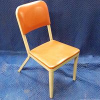 Full front view of mid-century chair showing orange naugahyde seat and backrest on beige metal frame.