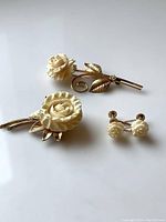 Photo of the full vintage floral jewelry set showing two gold filled brooches with carved cream roses and a pair of matching screw-back earrings.