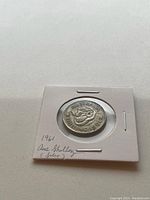 Front side of the 1961 Australian shilling showing the ram's head design and inscription 'AUSTRALIAN SHILLING 1961' with the coin enclosed in a white holder with handwritten notes indicating the year and silver content.