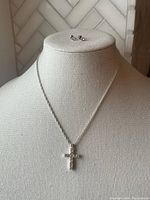 Front view of silver-tone necklace with cross pendant and matching stud earrings placed on mannequin bust.