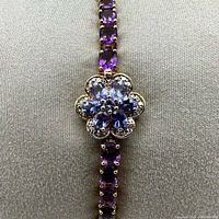 Close-up photo of the floral clasp featuring genuine tanzanite and topaz stones set in gold-plated sterling silver with adjoining amethyst stones.
