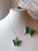 Photo showing necklace on display bust with butterfly pendant in green jade and rhinestones, ring on top of bust, and brooch pinned on bust side.