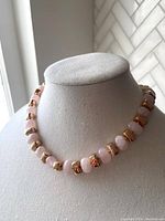 Front view of necklace displayed on a neutral fabric bust showing round rose quartz beads alternating with polished bronze square links.