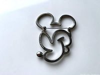 Back view of silver-tone metal outline brooch shaped as Mickey Mouse, showing the pin and clasp mechanism and engraved Disney logo.
