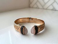 Front view of the rose gold plated hinged bangle showcasing twisted band texture and rose quartz ends with black spinel accents.