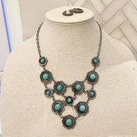 Full view of silver-tone necklace and matching earrings displayed on a mannequin bust, showing front view of necklace design and earrings resting on top.