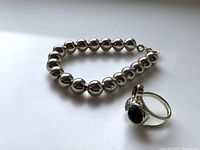 Photo showing silver-toned bracelet with spherical beads and size 8 ring with black stone and colored accents