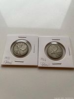 Two Canadian silver quarters from 1955 and 1956 in cardboard holders showing the reverse with caribou design and year labels.