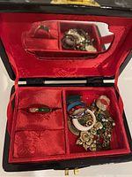Open jewelry box interior with red lining, showing compartments filled with rings and a jade bead bracelet