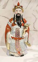 Front view of the full porcelain Fortune God statue showing detailed robe, facial features, and the missing portion of the hat.