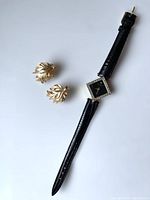 Full view of vintage Pierre Nicol quartz watch with black leather strap and matching pair of gold-tone Trifari earrings with leaf motif.
