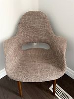 Front view of mid-century accent chair showing brown textured fabric upholstery with wear and fraying along edges, wooden tapered legs visible.