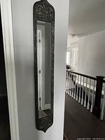 First photo showing one skinny vertical mirror mounted on a wall with ornate dark brass patina frame.