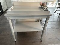 Front view showing overall structure: removable top tray, lower shelf, turned legs on brass casters.