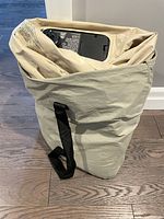 View of air mattress partially folded inside beige fabric bag with black handles on floor.