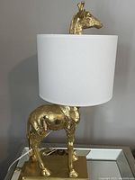 Full view of brass giraffe lamp with shade on mirrored surface