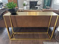 Front view of console table behind sofa showing overall shape and brass finish