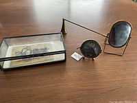 Shadow box, small round frame and mini antique mirror along with candle snuffer arranged on wooden surface