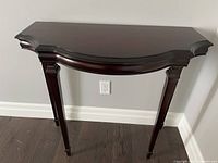 Front view of dark cherry foyer table showing half moon shape and bevelled edge top with four tapered legs on hardwood floor.