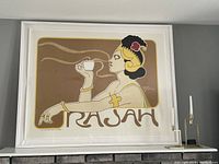 Framed vintage 'Rajah' tea advertising poster on a wall with white frame showing full composition including signature and steam design.
