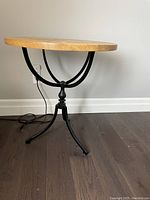 Side view of round mango wood table showing wood top and black metal legs with decorative curved support.