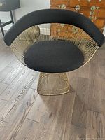 Front view of chair showing round black boucle seat and curved backrest on brass wire frame
