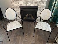 Front view of two black metal frame chairs with light quilted upholstery on seat and backrest, set by fireplace