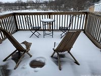 Deck view showing metal bistro table with glass top, two metal folding chairs, and two wooden folding Muskoka chairs under snow.