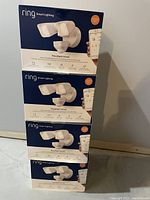 Four boxed units of Ring Smart Lighting Floodlight Wired stacked against a wall.