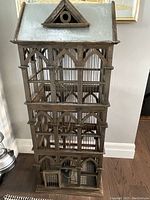 Front view of tall three-tier wooden bird cage with pointed arch detailing and pitched tin roof