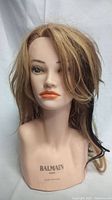 Blonde mannequin head with orange lipstick and BALMAIN Paris branding on the neck.
