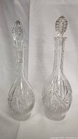 Two crystal decanters with matching stoppers, clear with detailed cut glass patterns.