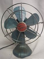 Front angle of Torcan blue metal desk fan with wire cage and five blades