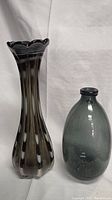 Two vases side by side showing the size difference, black and white swirl vase taller and to the left, grey rounded vase shorter and to the right.