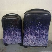 Photo showing front view of two luggage pieces with dark to light purple abstract pattern against white wall.