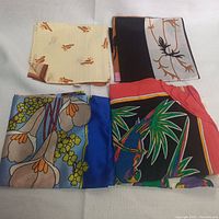 Four folded scarves showing different colorful and floral patterns including beige, black, blue, and multicolor designs.