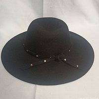 Wide-brim black felt hat with decorative studded band and bow, displayed on white background.